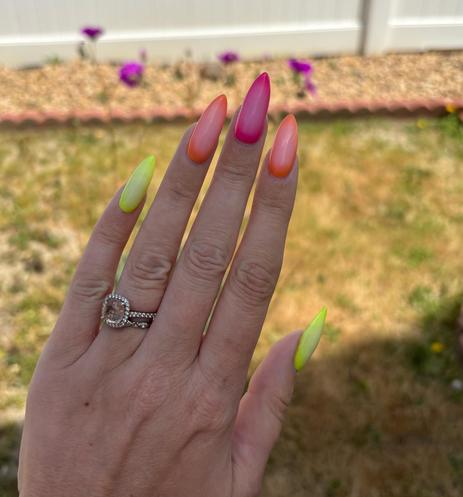 Yellow, orange, and pink acrylic nails against a blurry floral background