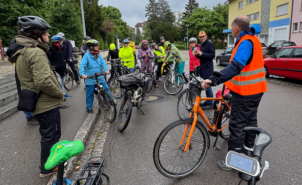 Eine Gruppe von Fahrradfahrern steht auf der Straße, während einer der Radler etwas erklärt.