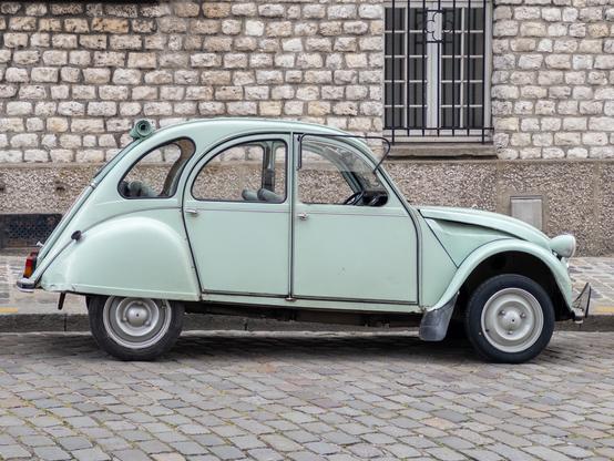 A vintage light green car parked on a stone street in front of a brick wall.