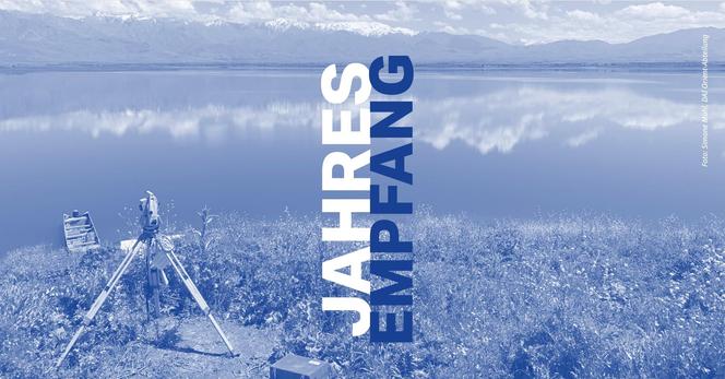 Blick über einen ruhigen See mit schneebedeckten Bergen im Hintergrund. Im Vordergrund steht ein Vermessungsgerät auf einem Stativ auf einer Wiese mit Wildblumen. Auf der rechten Bildseite steht vertikal der Schriftzug „Jahresempfang“. Foto: Simone Mühl, DAI Orient-Abteilung.