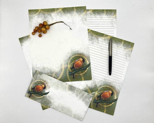 Product photograph of several pieces of illustrated stationery paper, featuring a Bullfinch image and pastel texturing with golden halos.