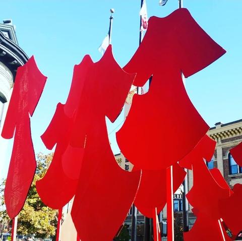 art installation  of multiple life-size wooden cutouts of red dresses on poles
