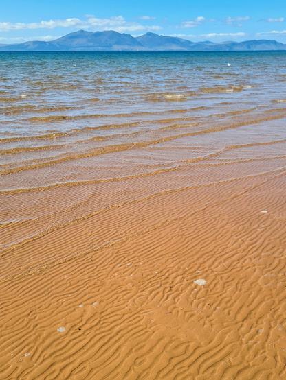 A view over a golden sandy beach and crystal clear turquoise waters to a distant mountainous island.