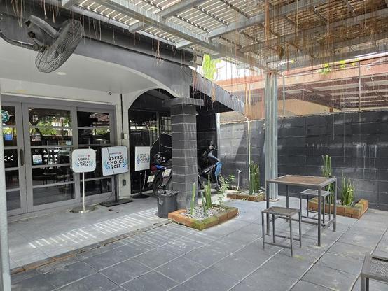 Outdoor seating area with metal table and stools, flanked by planters and a black wall.