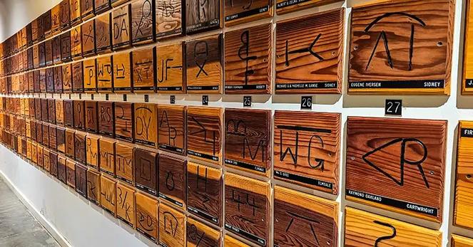 Wall covered with wooden placards providing area brands along with the name and location of the brand owner.