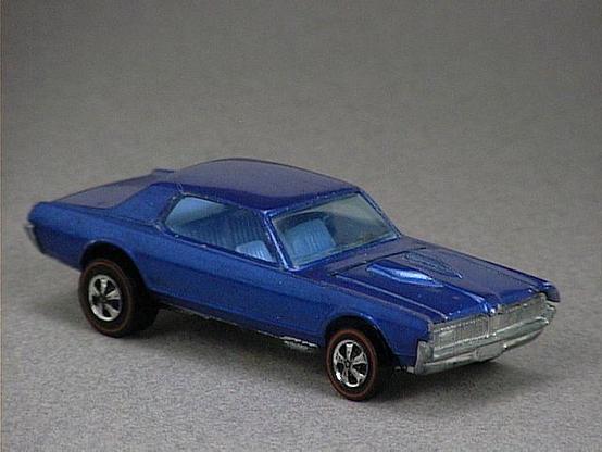 Released in 1968, Spectraflame Blue Custom Cougar of 1968 Hot Wheels with Redline wheels. Notes: US version has a dashboard, clear plastic windows and small steering heels. Available with or without painted roof, comes with a lift-up hood. Packaging: 1968 Blister. Metal Body, Metal Base. Made in USA. Scarcity: 5/10