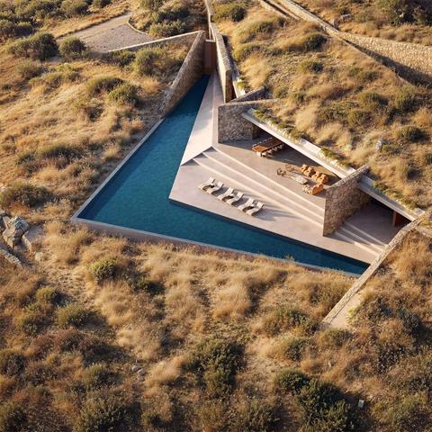 Aerial view of a modern, triangular swimming pool with lounge chairs and a stone terrace, surrounded by dry grass and shrubs.