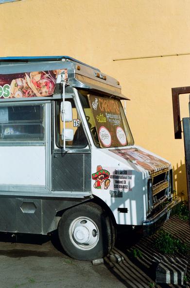 A closed Chevrolet taco truck sits parked in a lot behind an iron fence.