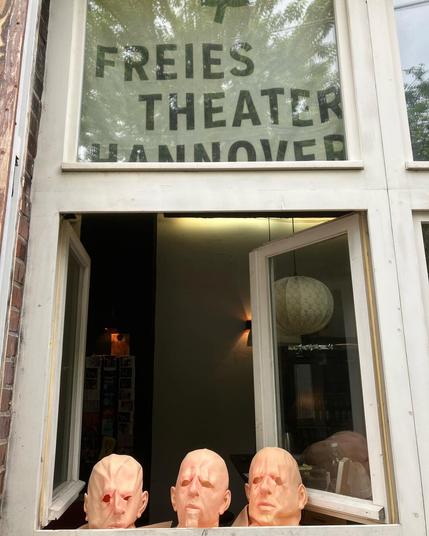 three bald head masks standing in an open window of a theatre.