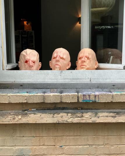 three bald head masks standing in an open window of a theatre.