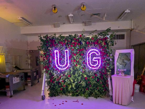 Our living wall covered in live greenery and roses, with a big pink neon UG on it