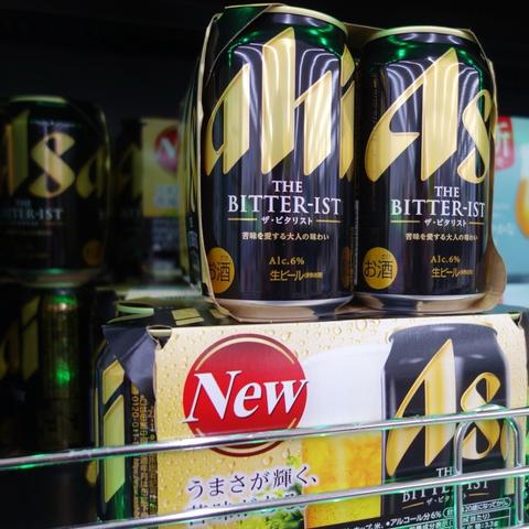 The image features a display of beer cans, prominently showcasing a product labeled "The BITTER-IST" with a 6% alcohol content. The packaging is predominantly black and gold, The cans are arranged in a metallic shelf