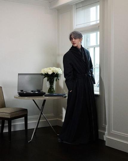 S.Coups ready to attend the Met Gala. He's in a hotel room standing by a window. There's an LP player and a bunch of flowers on the table behind him.