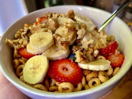 Heaping bowl of cereal that’s barely visible beneath layers of bananas, strawberries, blueberries, and walnuts.