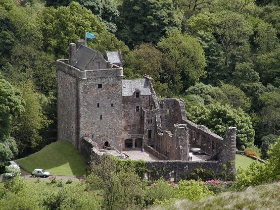 Castle Campbell. The image shows a view steeply down onto a tower house castle with the tower house in the far-left corner and a range of buildings to its right and another, though roofless, extending along the left side of the square form of the castle. The square is complete by walls on the near side and partly on the left. The background is full of trees on a rising slope.