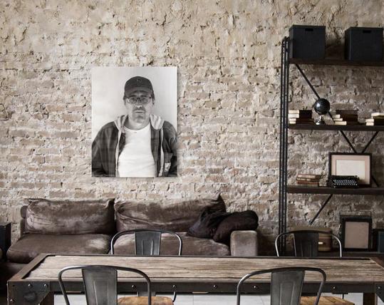 Self portrait of a photographic artist in work clothes on the wall of a rustic room.