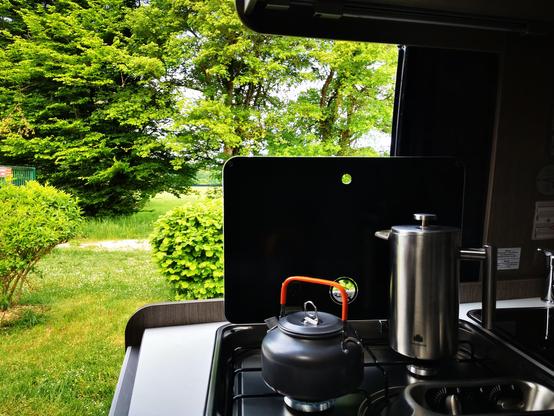 Blick aus der offenen Schiebetür ins Grüne. Auf dem Herd kocht der Wasserkessel und die French Press steht daneben.