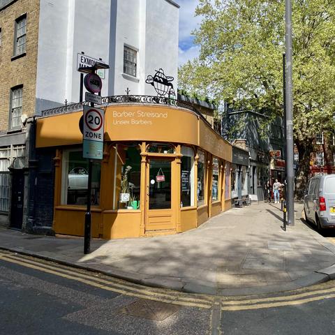 A colorful barbershop named "Barber Streisand", somewhere in Exmouth Market in London, during a sunny morning.