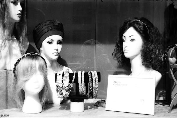 Schwarzweißfoto, das einen Ausschnitt aus dem Schaufenster eines Ladens zeigt, der Perücken und Kopfschmuck anbietet. Vier Mannequin-Büsten tragen einen Teil der angebotenen Produkte. In Bildmitte ist auch der Fotograf undeutlich als Spiegelbild sichtbar. Leica IIIg mit 50 mm Summitar auf Adox Scala-Diafilm.