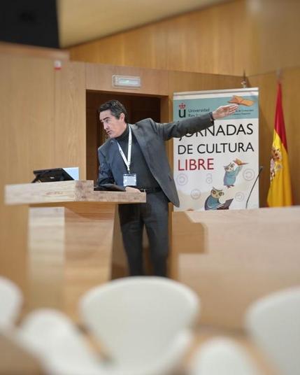 Un hombre presenta en una conferencia, hablando frente a una audiencia atenta