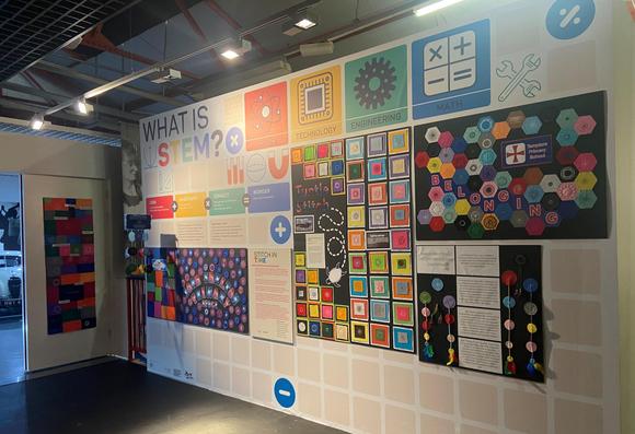 A display from the Stitch in Time project in 2024. This is a wall in the Coventry Transport Museum. On the wall are a number of different displays, showing the work of primary school students. The displays have coloured felt patches, and on each patch is a stitched pattern.
