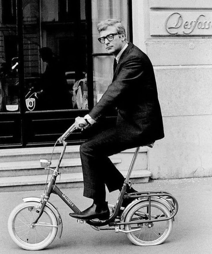 Michael Caine riding a small bicycle