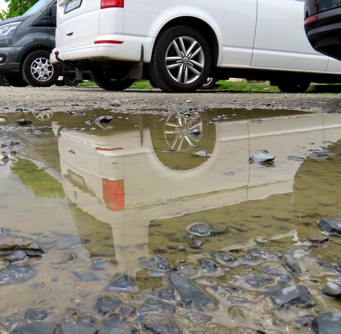 In einer Pfütze spiegelt sich ein Teil eines weißen Autos