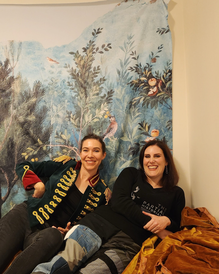 Image one: Dr G and Dr Rad are lying down on a couch together while laughing.