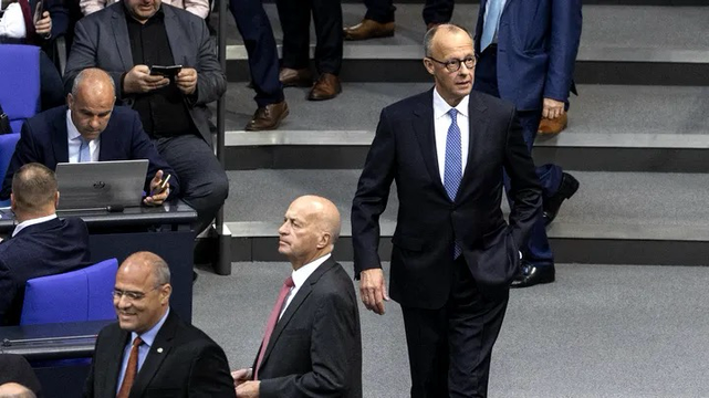 Merz im Plenarsaal wie er entlang von Abgeordneten geht
