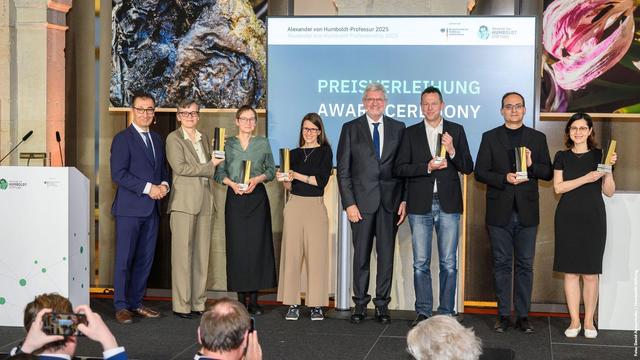 Foto: Preisverleihung der Alexander von Humboldt-Professur 2025, mehrere Personen stehen auf einer Bühne und halten Preise in den Händen, ein großer Bildschirm zeigt 'Preisverleihung - Award Ceremony'.