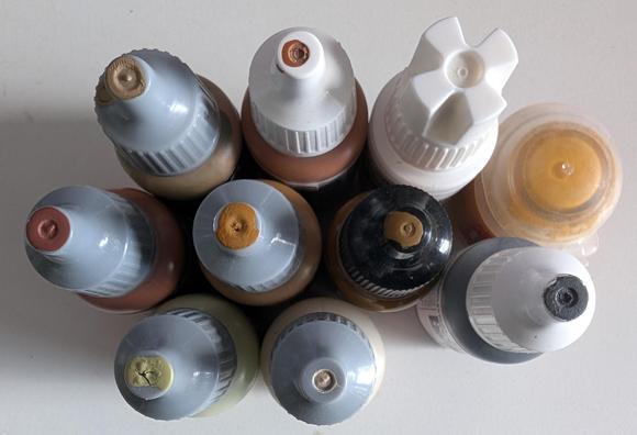Ten bottles of acrylic miniature paints, with different shades of brown, plus grey and white.