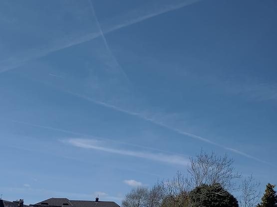 Seen above local rooftops a cloudless blue sky criss-crossed with contrails, that are slowly dissipating. In the upper left quadrant of the image 2 overlapping contrails, with the blue sky background,  make a passable representation Saltire of Scotland