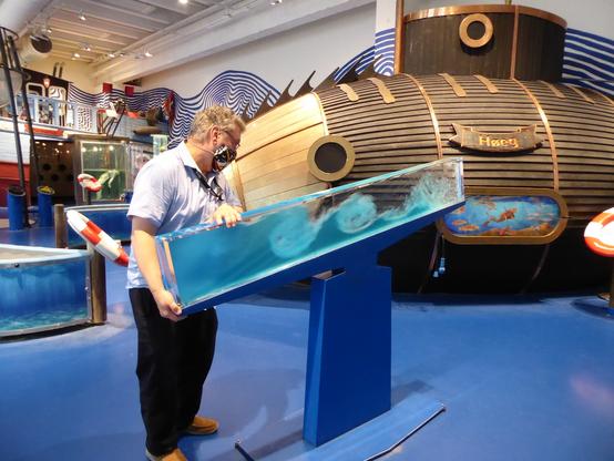 In the foreground, a long, clear plexiglas chamber filled with immiscible blue and clear liquids. When tilted, waves were generated that simulated surf, tide, etc. In the background there is a bathysphere, a sort of wooden submarine.