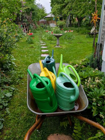 Schubkarre mit bunten Gießkannen in Grün, Gelb und Türkis steht auf einer Wiese im Garten, im Hintergrund ein romantischer Gartenweg mit Trittsteinen, Tulpen, Vogeltränke und Bäumen.
Foto by Johann Seidl, Gartenpoet.


A wheelbarrow filled with colorful watering cans in green, yellow, and turquoise stands on a lawn in a lush garden; in the background, a romantic garden path with stepping stones, tulips, a birdbath, and trees.
Photo by Johann Seidl, Gartenpoet.