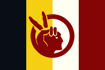 Flag of the American Indian Movement, with black, yellow, white and red vertical stripes. At the center is a sketch of an Indigenous person with a hand on its head, making the Peace Sign in a way that also looks like a feathered head dress.