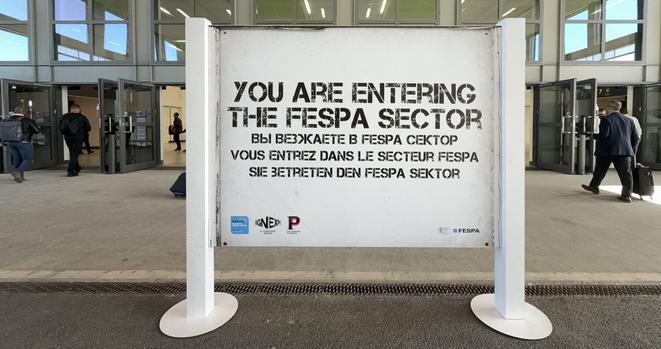 Angelehnt an das berühmte Berliner Mauerschild „You are leaving the American sector“ begrüßt die FESPA ihre Gäste mit einem Augenzwinkern: „You are entering the FESPA sector“.
Die Anspielung sitzt – in vier Sprachen, mit Retro-Charme und der vollen Wucht grafischer Gestaltung.
Kein Wunder: Die Messe ist aus einer Siebdruckfachmesse hervorgegangen und heute die weltgrößte Bühne für Druck, Textil & Werbetechnik.
Wer hier durch die Tür geht, betritt nicht nur einen Sektor – sondern eine ganze Branche im Hochformat.