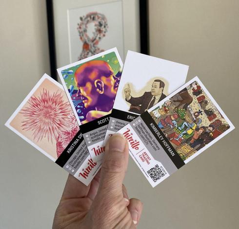 A hand holds four illustrated business cards, each with different artwork and names, in front of a blurred framed picture on a beige wall.