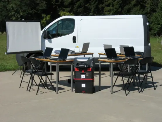 Tables et chaises et matériel informatique du CMI installés devant un utilitaire blanc.
