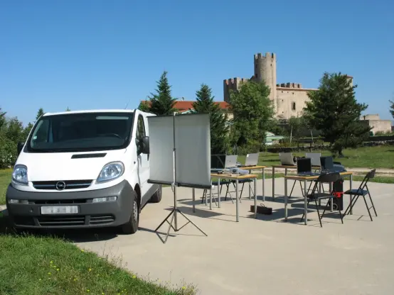 Tables et chaises et matériel informatique du CMI installés à côté d'un utilitaire blanc, devant le château d'Essalois
