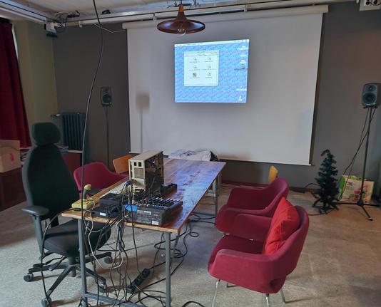 table with chairs around it. on the table is a Macintosh IIci and some peripherals. a projector is displaying the Mac's desktop with a single folder open.