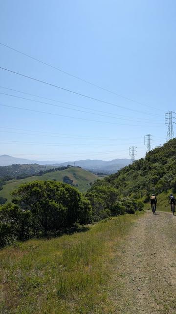 Two bicycle riders descending a dirt road, green hills, blue sky