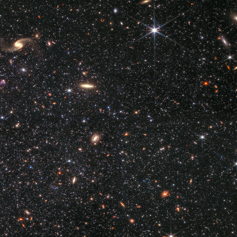 Thousands of clearly differentiated objects of various color, size, shape, and brightness. Most of the objects are points or solid circles of reddish-orange, blue, or white light. These are the stars that make up the WLM galaxy. A few blue-white foreground stars with Webb’s distinct 8-pointed diffraction pattern, and a number of spiral and disk-like background galaxies are also visible.