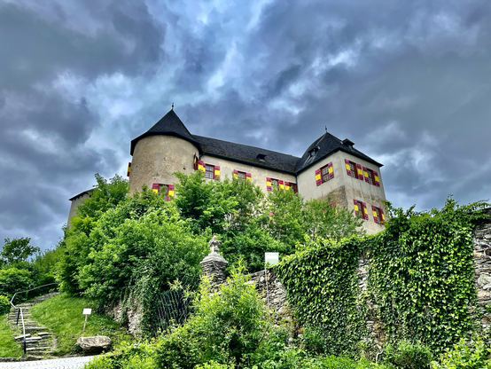 Burgmauer mit grünem Efeu verwachsen und eine Ritterburg dahinter mit bedrohlich dunklen Wolken