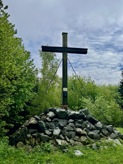 Gipfelkreuz auf Steinen errichtet mit grünen Wäldern rundum