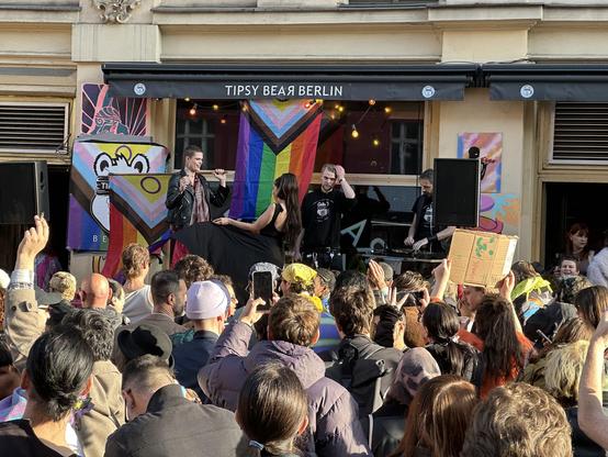 Spontandemo nach Angriff auf queere Bar in Prenzlauer Berg. Im Vordergrund Menschen. Im Hintergrund klein Bühne und Musik