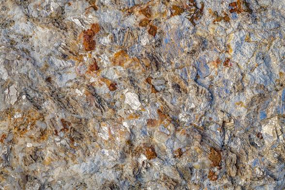 Close-up photo of a grey rock surface with large glittering mica flakes and orange-brown garnet