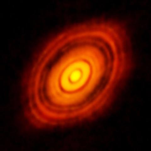 The first ALMA image of the HL Tauri protoplanetary disk. The image color palette orange and red, with more emission in brighter colors. Grooves can be seen in the disks where protoplanets have been eating away at the material.