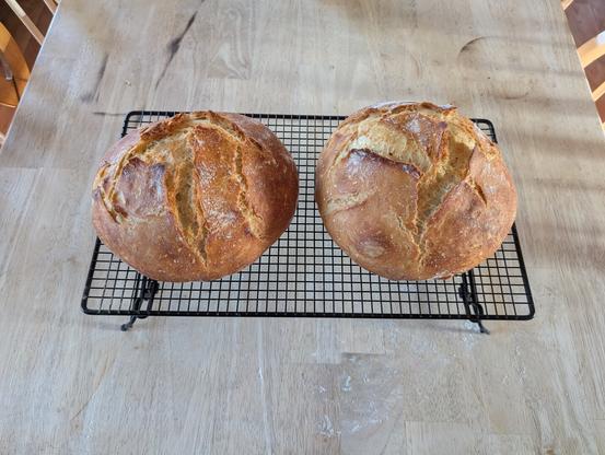 Two round loaves of golden brown bread on a black metal cooling rack, on a wooden surface.