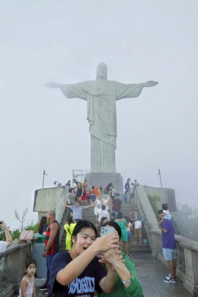 On the foggy Corcovado, two woman are doing a selfie in front of the Christ's statue while there is a breach in the clouds and we can actually see the statue.