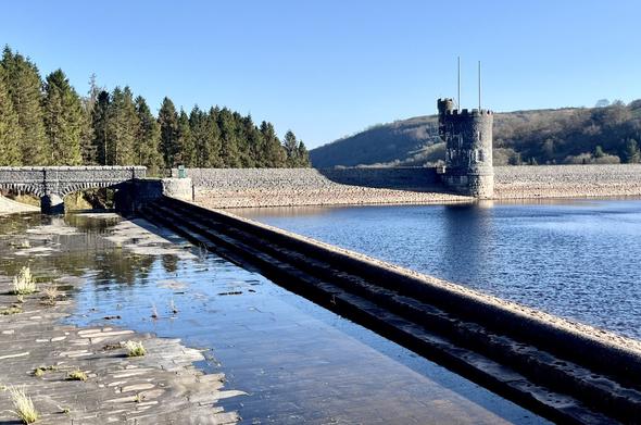 Very still water, with puddles in a spillway in the foreground. There is a turret on the dam in the middle distance.